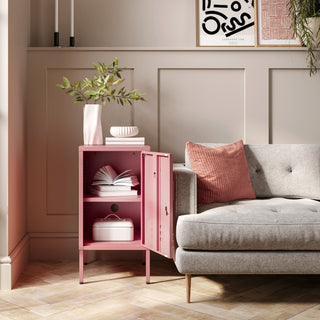 The Camden flamingo pink metal storage locker open as a side table next to a sofa