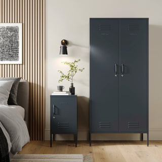 The Chelsea tall double-door metal storage locker and The Camden side table locker both in slate grey, next to each other in a bedroom