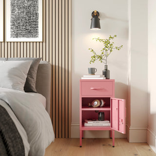 Metal side table locker in flamingo pink with one drawer and one door open showing books, in a room next to a bed