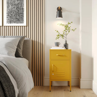 Metal side table locker in mustard yellow with one drawer and one door, in a room next to a bed