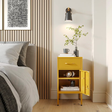 Metal side table locker in mustard yellow with one drawer and one door open showing books, in a room next to a bed