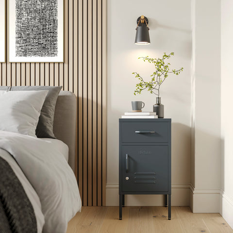 Metal side table locker in slate grey with one drawer and one door, in a room next to a bed