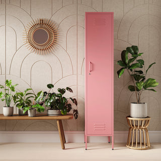 The Bexley single-door tall storage locker in flamingo pink, next to some plants