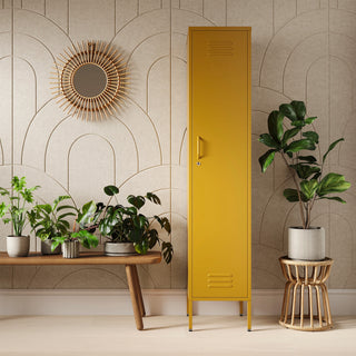 The Bexley single-door tall storage locker in mustard yellow, next to some plants